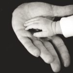 A black and white photo where a child's hand rests in an adult's hand.